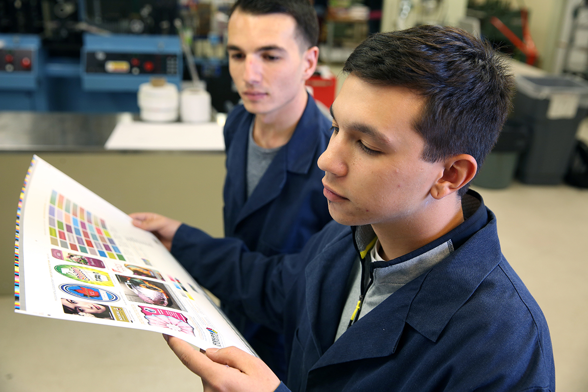 A graphic communications student inspects a press sheet. Students in the fall will be able to use a new digital press, quality control software and a spectrophotometer.