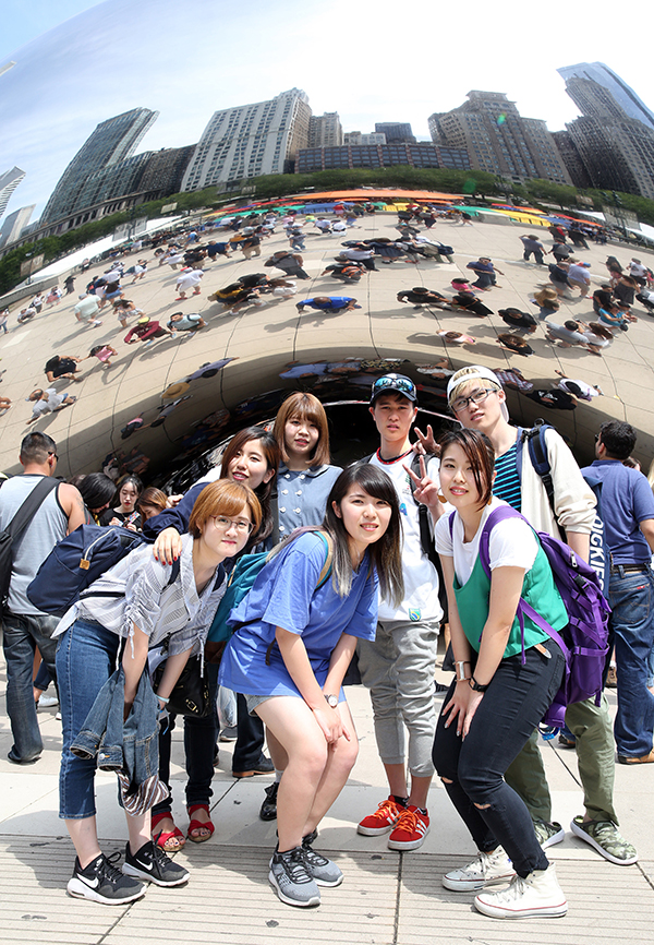 International students at UW-Stout huddle under the Cloud Gate sculpture in Chicago’s Millennium Park. The Michigan Avenue skyline is reflected above them.