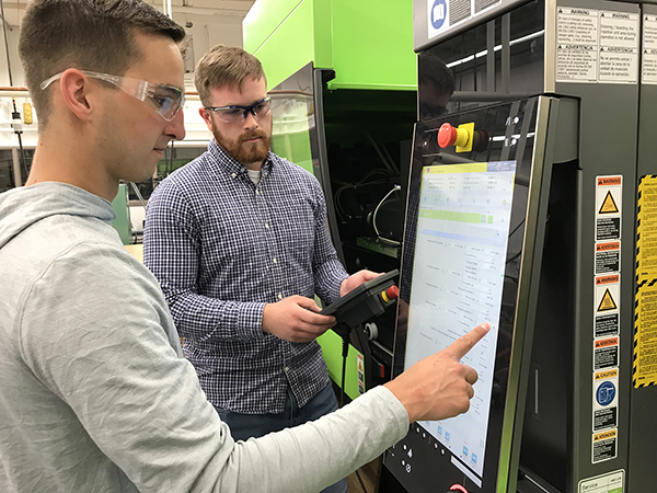 Jacob Malinowski, left, and Austin Braden program the injection molding machine.