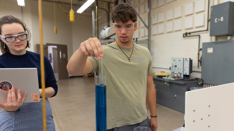 A student dipping a class cylinder into a tall beaker of blue liquid